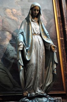 a statue of the virgin mary in front of a painting