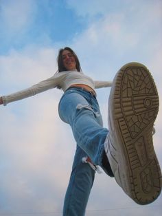 a woman in white shirt and jeans doing a trick on a skateboard with her feet