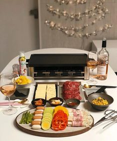 an assortment of meats, cheeses and vegetables on a table with wine glasses