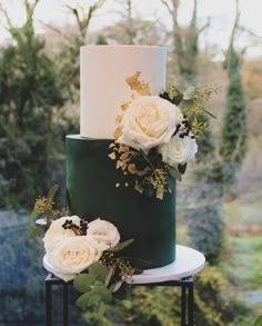 a three tiered green and white wedding cake with flowers on the top, surrounded by greenery