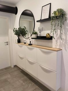 a white dresser with two mirrors and plants on the top shelf in front of it