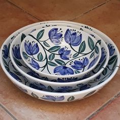 three blue and white bowls sitting on top of a tile floor