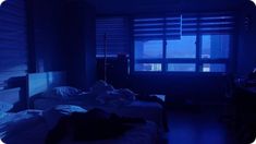 two beds in a dark room with blue light coming from the window and curtains on the windowsill