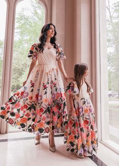 a mother and daughter standing in front of an arched window wearing dresses with flowers on them