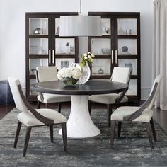 a dining room table with chairs around it and a vase on the table in front of bookshelves