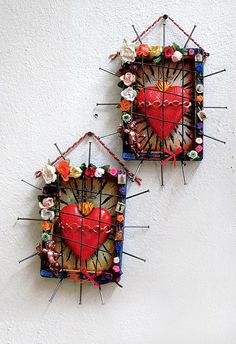 two pieces of art made out of sticks and paper with flowers on them, hanging from the side of a wall