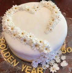 a heart shaped cake decorated with daisies and gold lettering that reads golden year 50