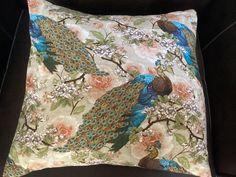 a decorative pillow with two peacocks on the front and back, sitting on a black chair