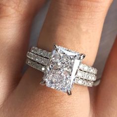 a woman's hand with a diamond ring on top of her wedding band and an engagement ring in the middle