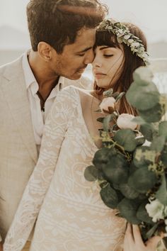 a man and woman embracing each other with greenery around their necks in front of them