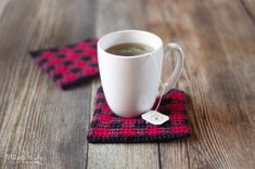 a cup of coffee sitting on top of a wooden table next to a red and black coaster