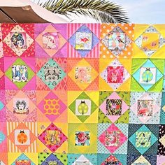 a colorful quilt hanging on the side of a building next to a palm tree in front of it