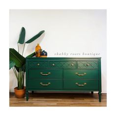 a green dresser sitting next to a potted plant on top of a hard wood floor