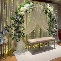 a white and blue wedding ceremony setup with flowers on the back wall, draped drapes, and a bench