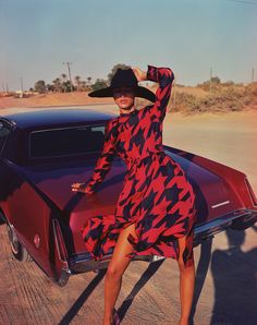 a woman in a red and black dress leaning on the hood of a car