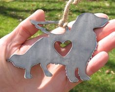 a hand holding a metal dog ornament with a heart in the shape of a dachshund