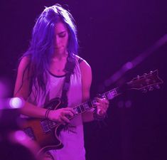 a woman with blue hair playing an electric guitar in front of purple lights on stage