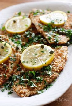 a white plate topped with chicken covered in herbs and lemons on top of a wooden table