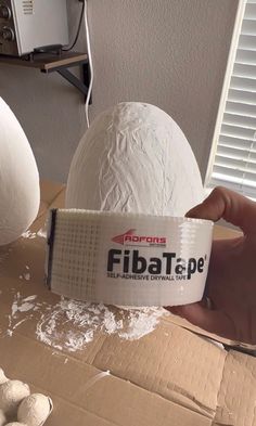 a person is holding up a paper mache in front of some white eggs on a cardboard box