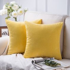 two yellow pillows sitting on top of a white couch next to a vase with flowers