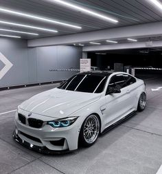 a white car is parked in an empty parking garage with its hood up and lights on