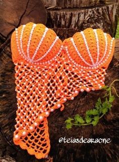 an orange and white crocheted headband with pearls on it sitting next to a tree stump