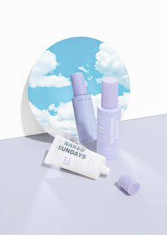 an assortment of skin care products sitting on a white surface with blue sky and clouds in the background