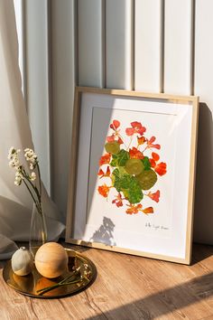 an art work is displayed on a table next to a vase with flowers in it