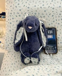 a blue stuffed animal sitting on top of a bed next to an ipod and headphones