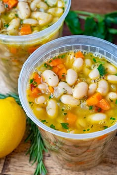 two plastic cups filled with soup next to lemons and parsley on a wooden table