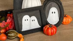 two framed pictures with ghost faces and pumpkins in front of them on a table