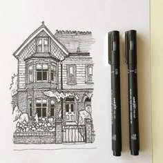 two black pens sitting on top of a piece of paper next to a drawing of a house