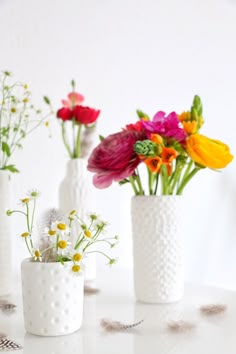 three white vases filled with colorful flowers on top of a table next to each other