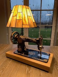 an old sewing machine lamp sitting on top of a wooden table next to a window