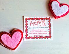 two felt hearts sitting next to each other on a white table with a card in the middle