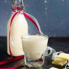 a bottle of milk next to a glass with some cheese on it and a red ribbon