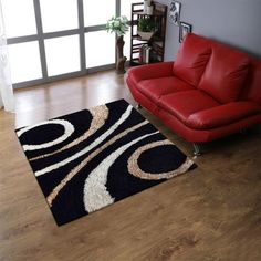 a living room with a red leather couch and black area rug on the hardwood floor