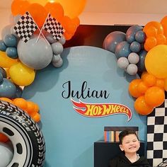 a young boy sitting in front of a car themed backdrop with balloons and race cars