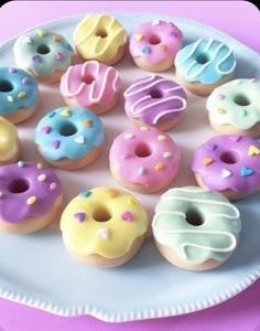 a white plate topped with lots of different donuts on top of a pink table