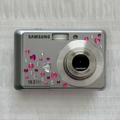 a silver camera with pink and white jewels on it's front side, sitting on a white surface