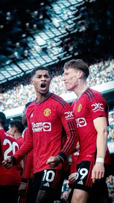 two men in red uniforms standing next to each other on a soccer field with fans watching