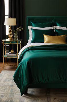 a green bed with white and gold pillows in a dark colored room, next to a black curtained window