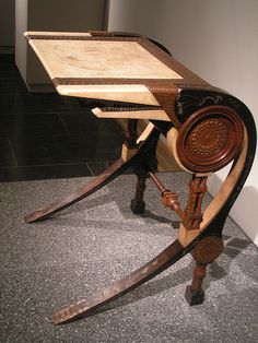 an old wooden desk sitting on top of a gray floor next to a white wall