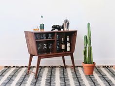 a wooden cabinet with wine glasses on it next to a cactus