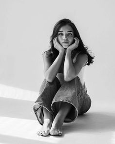 a black and white photo of a woman sitting on the floor with her hands under her face