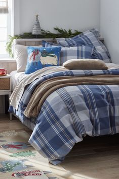 a bed with plaid comforter and pillows in a bedroom next to a christmas tree