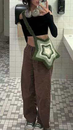 a woman taking a selfie with her cell phone in a public restroom while wearing brown pants and a black crop top