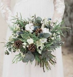 a bridal holding a bouquet of flowers and greenery with pine cones on it