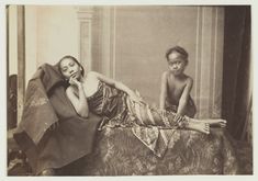 an old black and white photo of two women sitting on a bed with one laying down