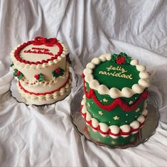 two decorated cakes sitting on top of a white cloth covered tablecloth, one is green and the other is red